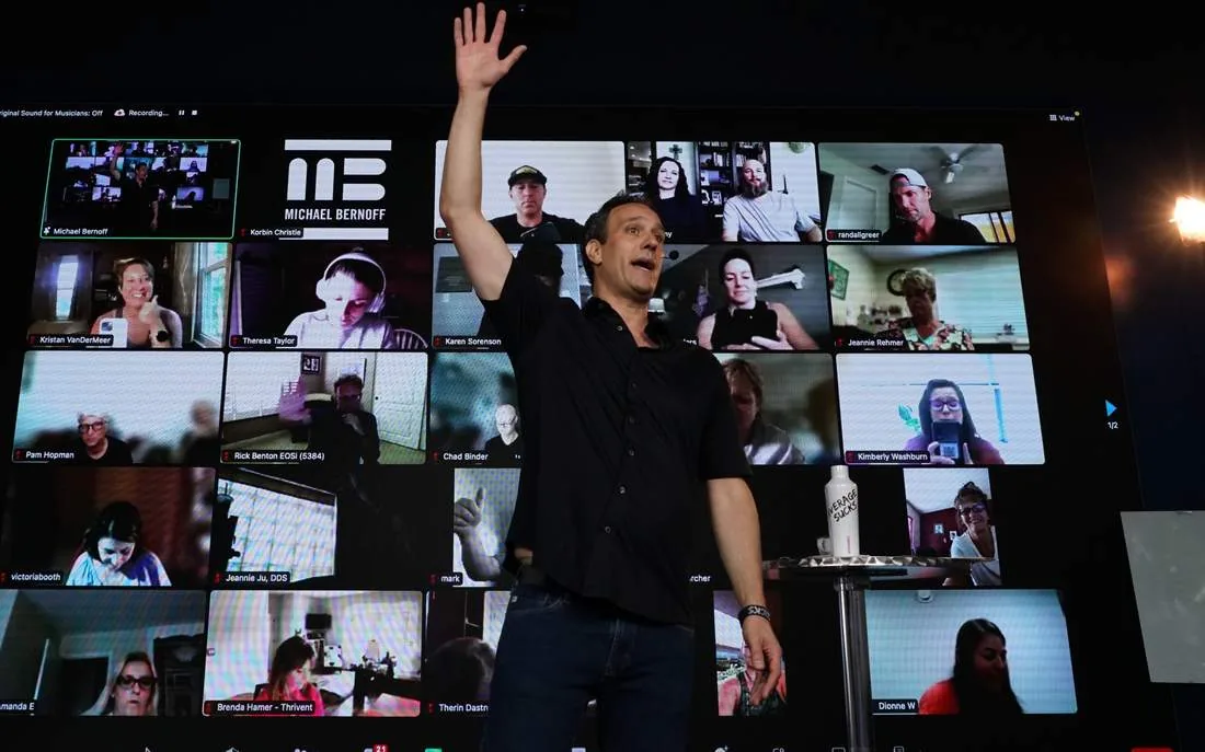 A speaker presenting live in front of the LED wall filled with remote attendees
